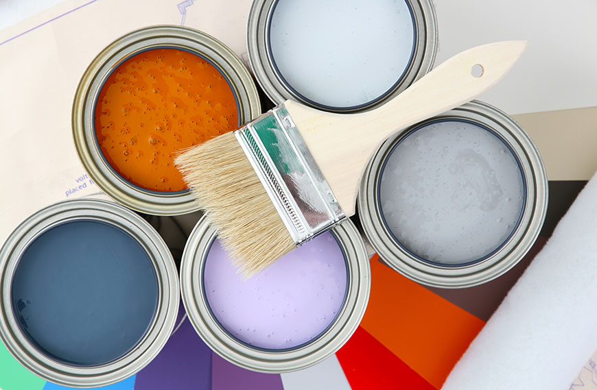 Image of colorful paint cans with brush on top.